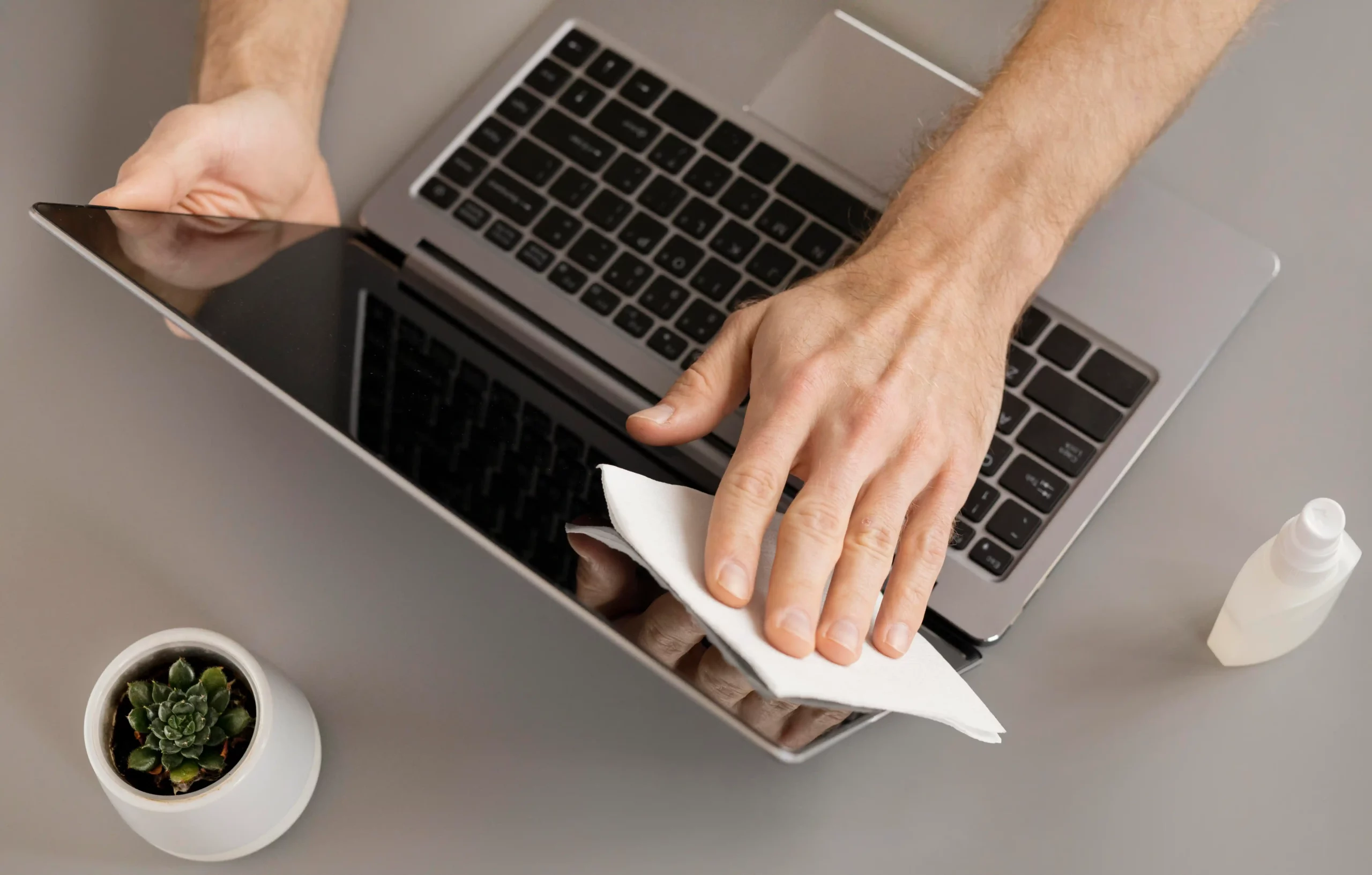 A person cleaning a laptop screen with a microfiber cloth to extend laptop lifespan by reducing dust and improving cooling.