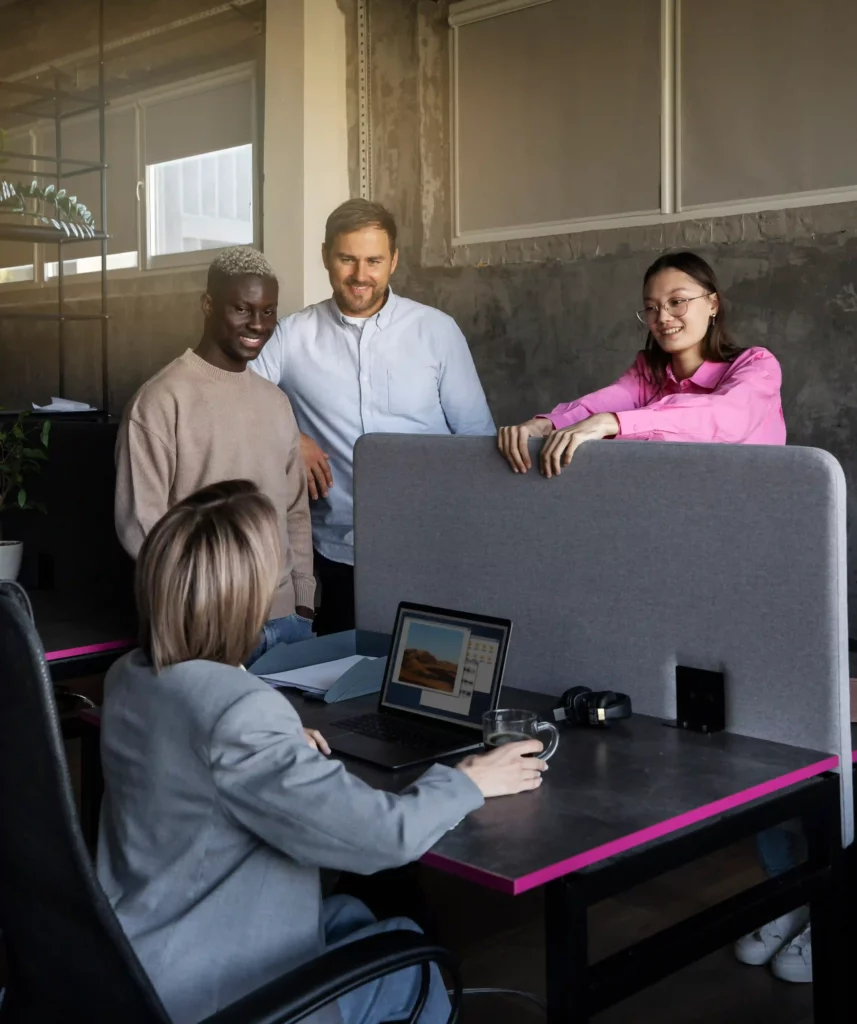 A diverse team of professionals collaborating in a modern New Jersey office environment, with one person receiving IT assistance at a desk while others offer support and ideas.