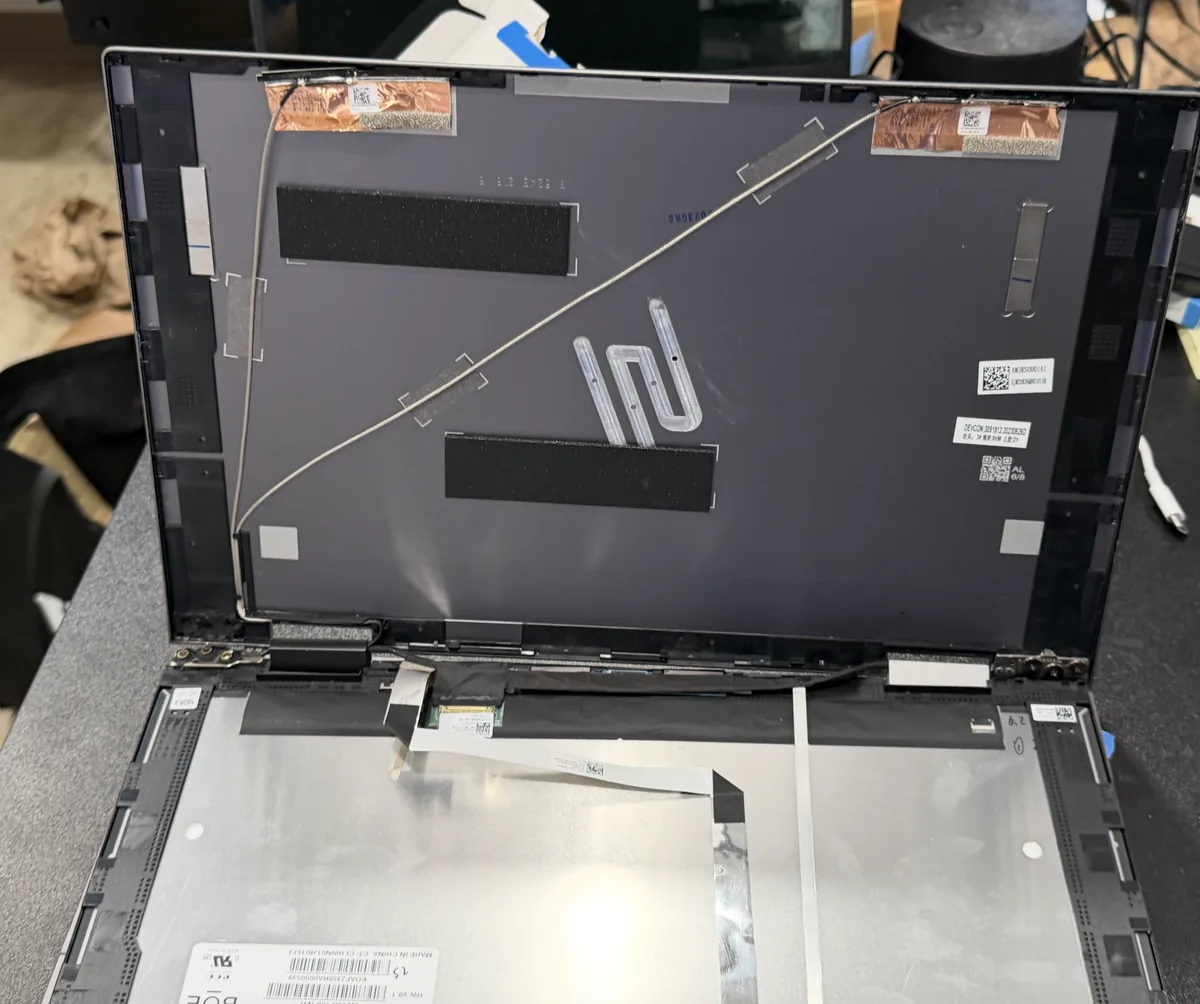 Laptop screen replacement in progress with the display shell open and a new LCD panel staged on the bench